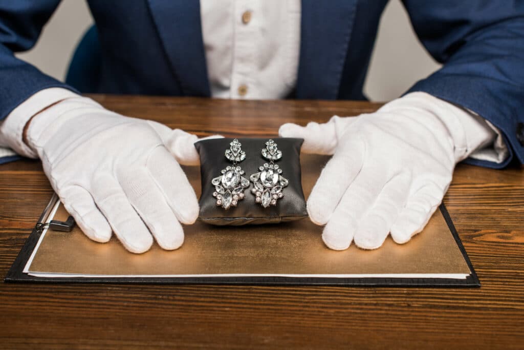 a jewelry appraiser in white gloves assessing the value of a pair of dangle earrings